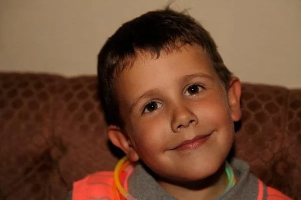 Young Jamie smiling at the camera with a glow stick around his neck.