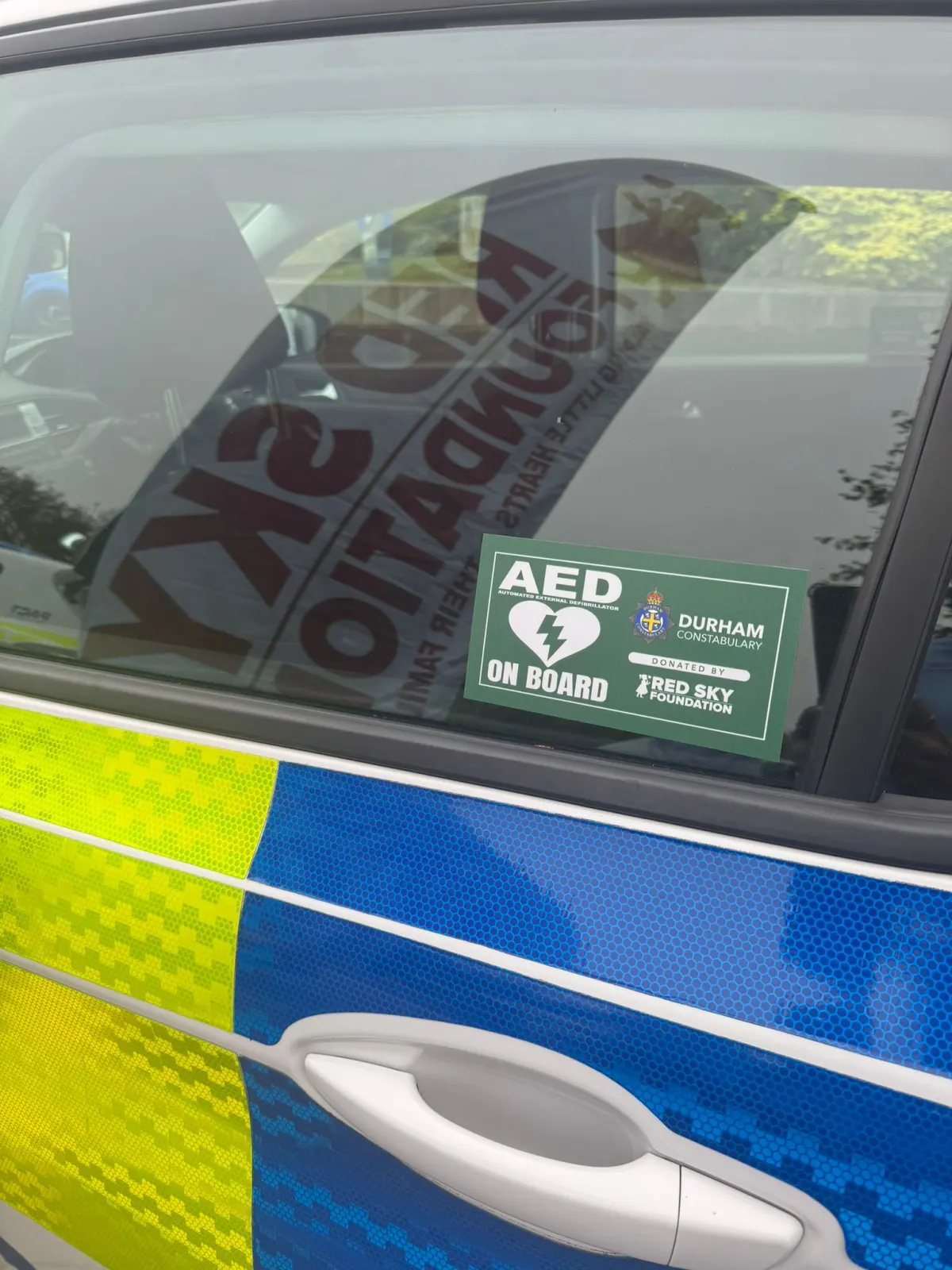 An 'AED on Board' window decal on a police vehicle, carrying Durham Constabulary and Red Sky Foundation marks.
